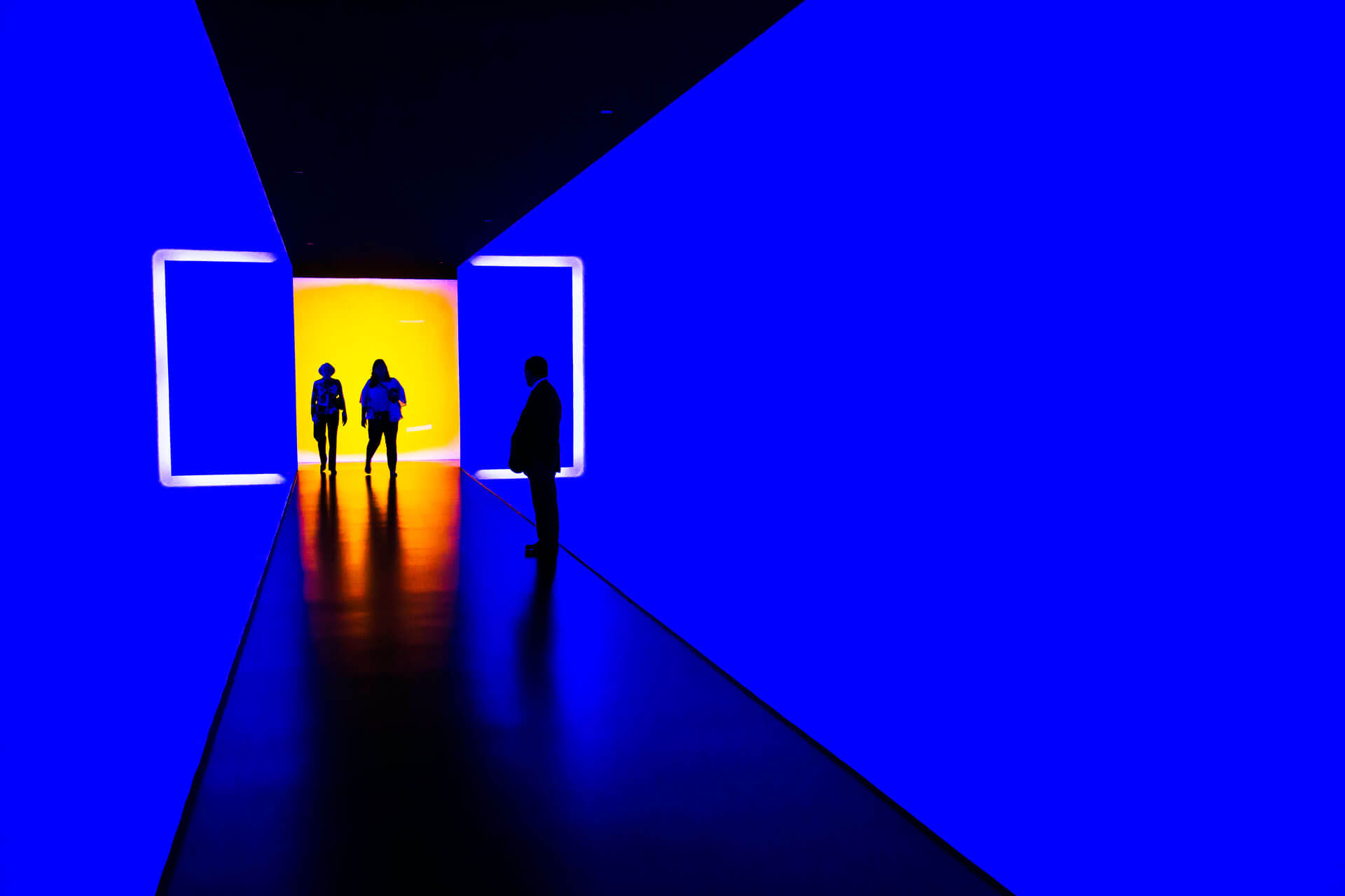 three people standing near very blue wall inside building